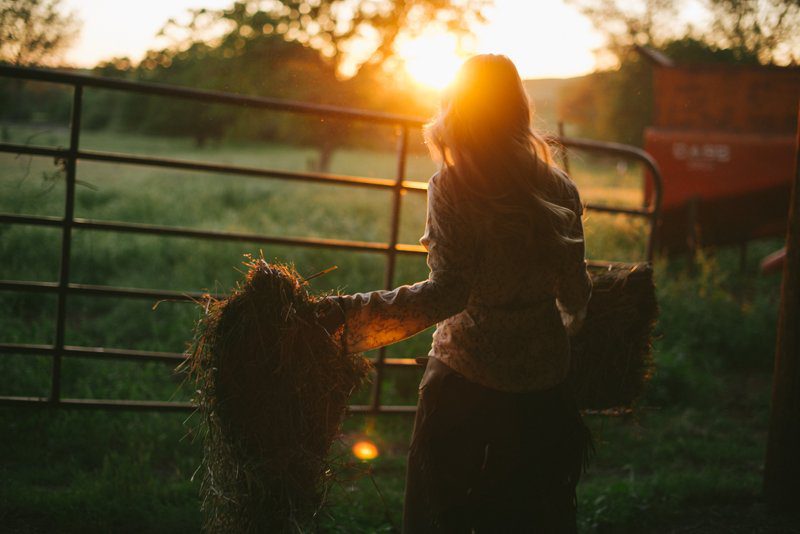 lifestyle-portrait-of-woman-moving-hay-at-sunset